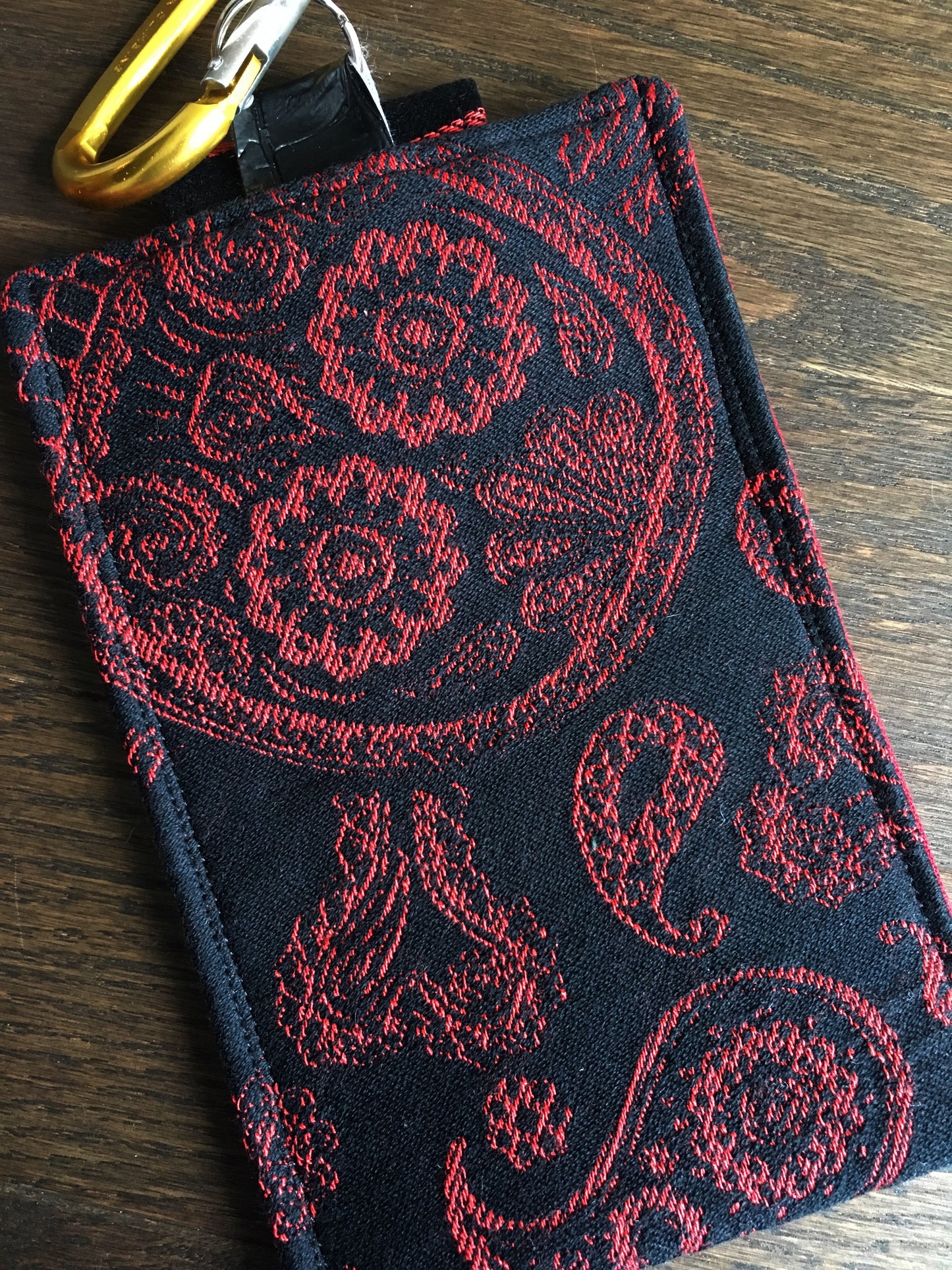 Image of a handmade and pirate themed phone pouch. It features skelewag fabric from Alexander Henry, bold red and black skull and crossbones woven jacquard fabric, an internal card pocket, and a belt or purse clip.