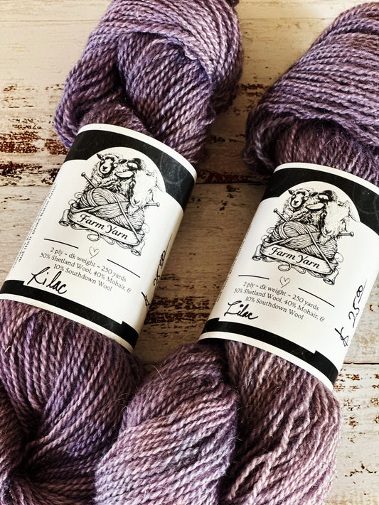 Two skeins of purple yarn with labels on a wooden surface