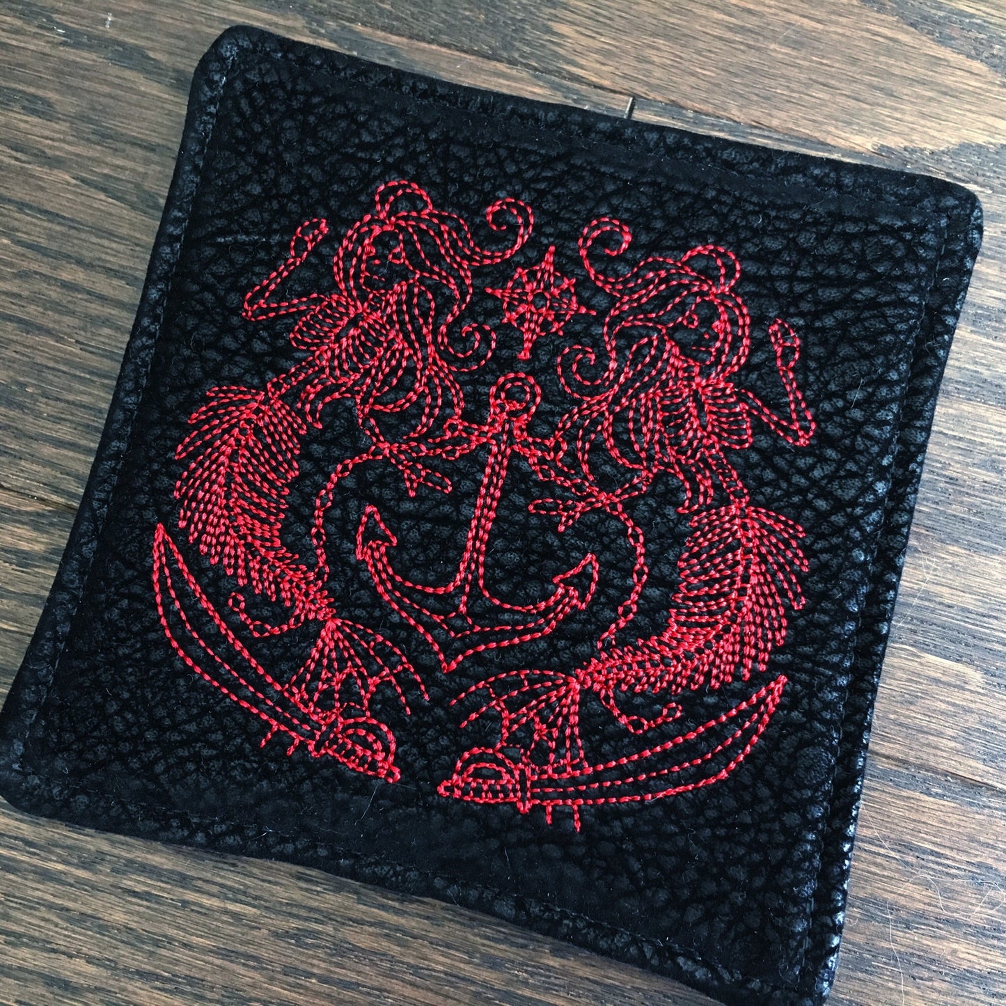 Image of a bold and handmade pirate themed mug rug. It features red and black paisley skull wrap scraps on one side and a blood red pirate mermaid crest embroidery design on the reverse.