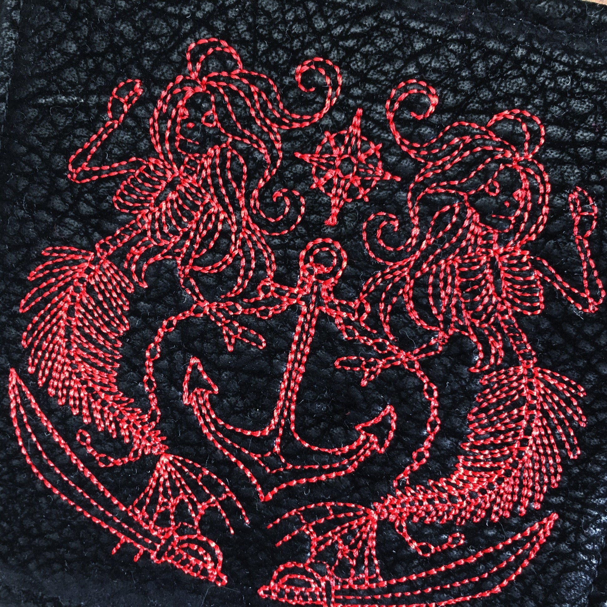 Image of a bold and handmade pirate themed mug rug. It features red and black paisley skull wrap scraps on one side and a blood red pirate mermaid crest embroidery design on the reverse.