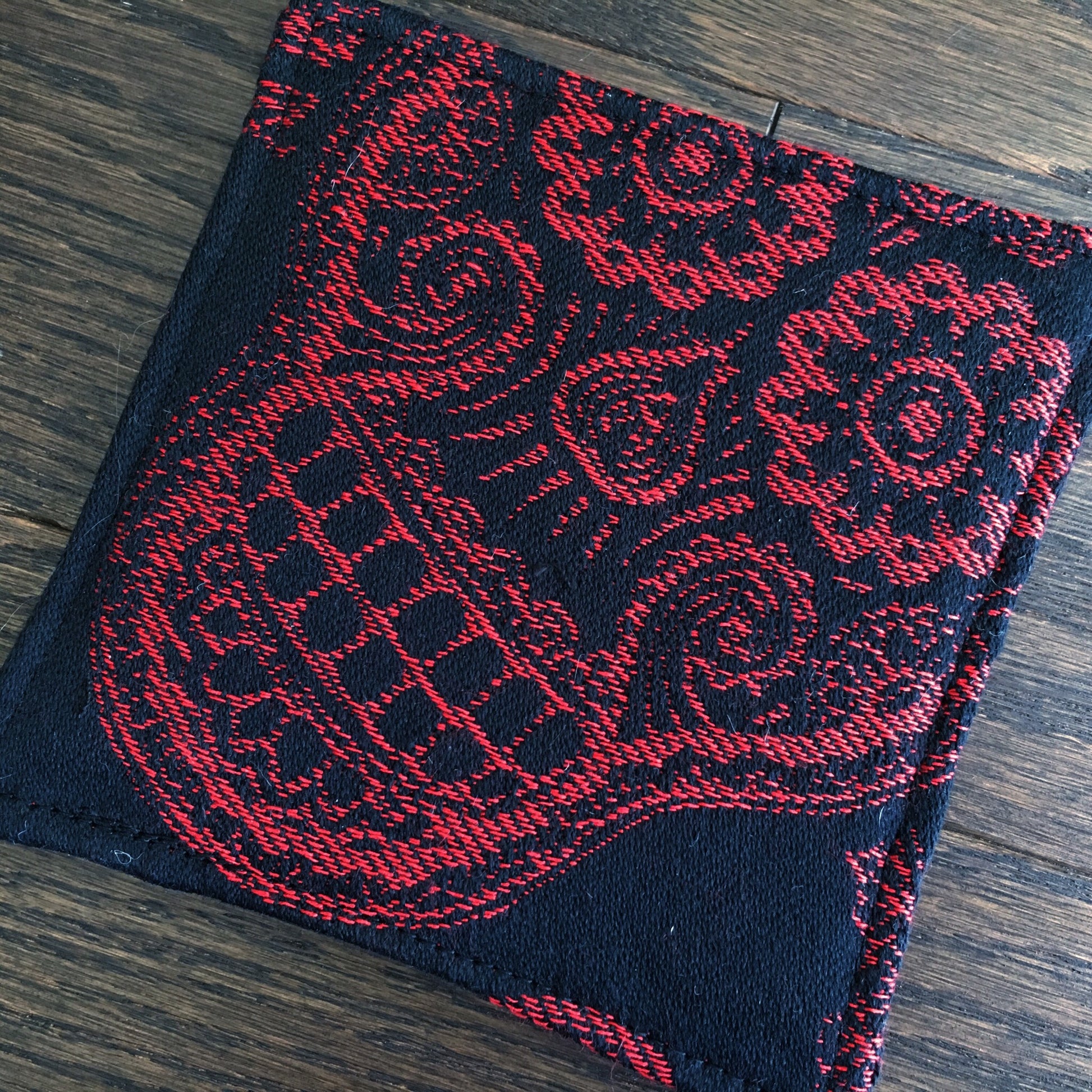 Image of a bold and handmade pirate themed mug rug. It features red and black paisley skull wrap scraps on one side and a blood red pirate mermaid crest embroidery design on the reverse.