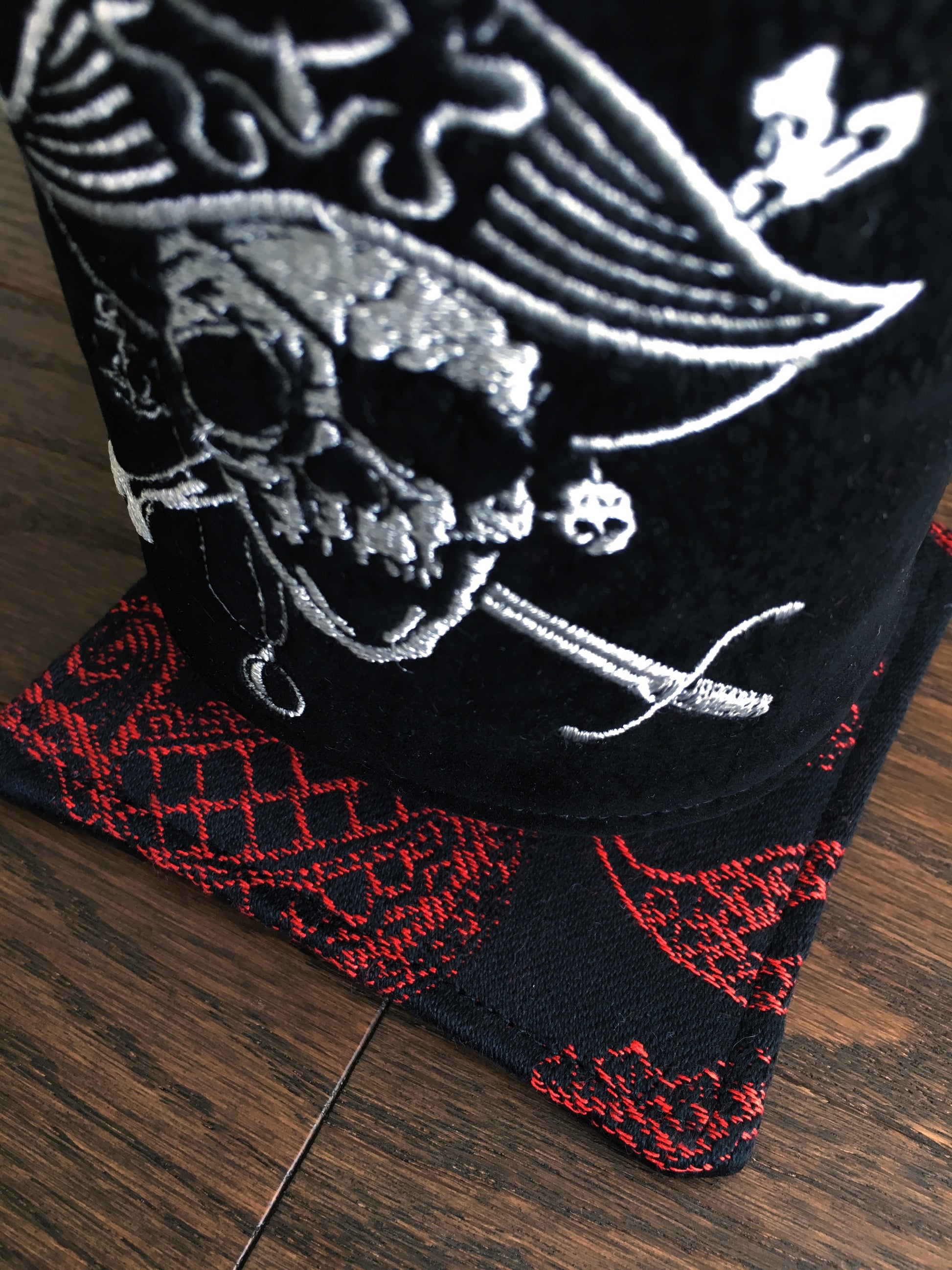Image of a bold and handmade pirate themed mug rug. It features red and black paisley skull wrap scraps on one side and a blood red skull and crossbones embroidery design on the reverse.