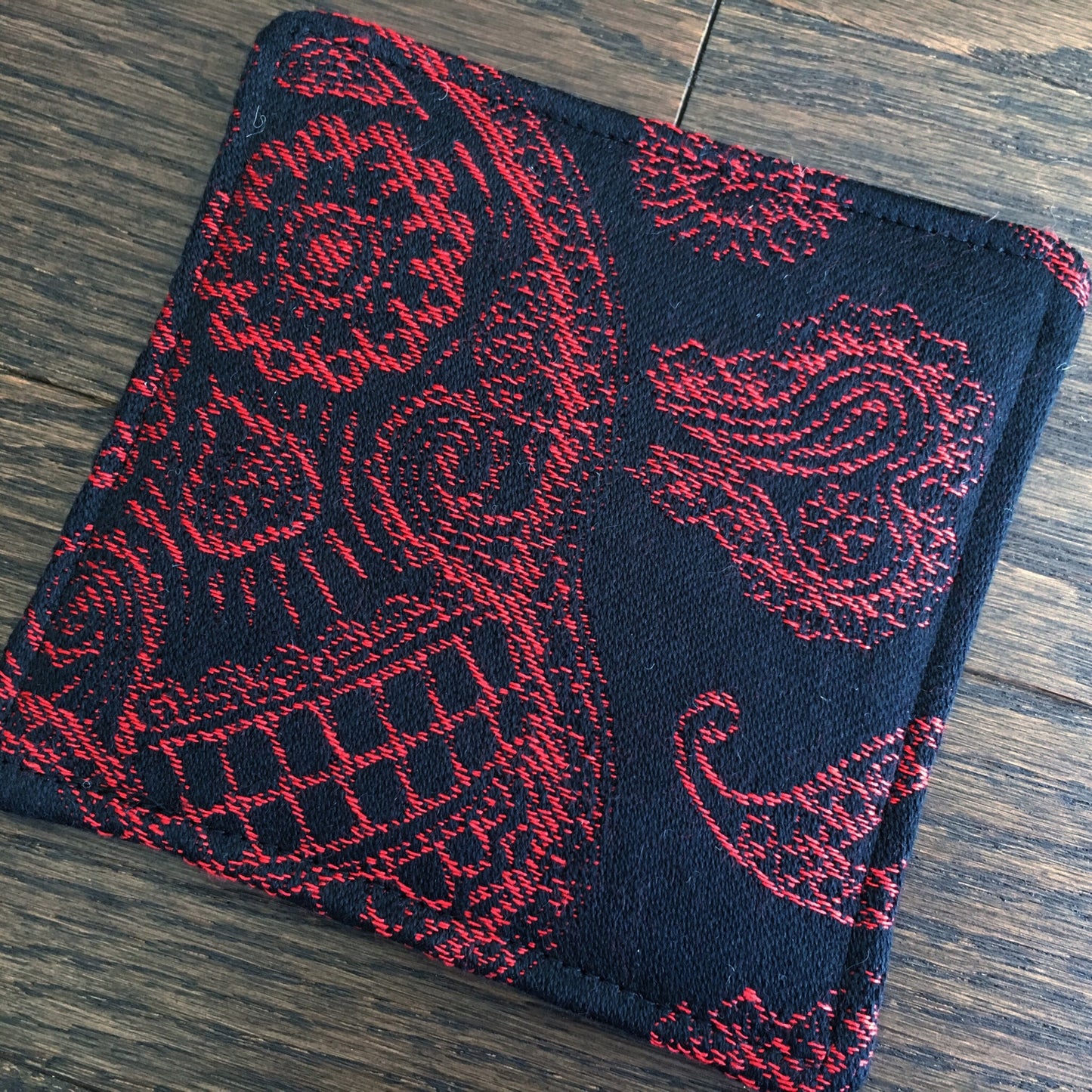 Image of a bold and handmade pirate themed mug rug. It features red and black paisley skull wrap scraps on one side and a blood red skull and crossbones embroidery design on the reverse.
