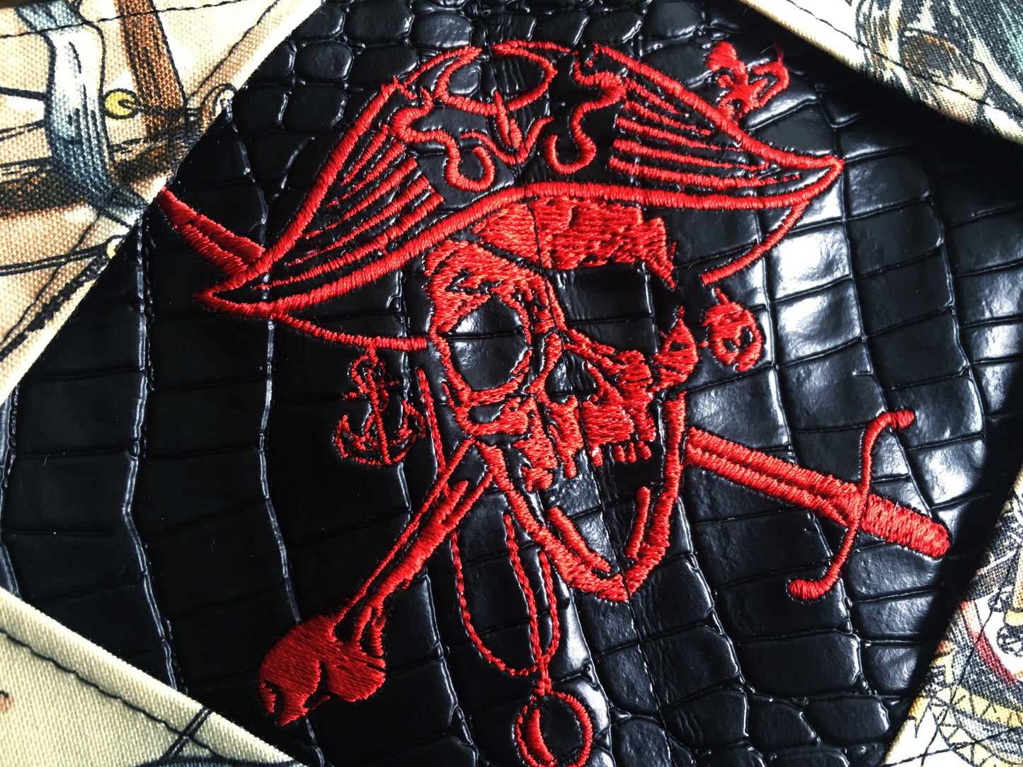 Image of a handmade and pirate themed mini card wallet made from red and black jolly roger woven textile, skelewag fabric, and black faux leather. It features a machine embroidered skull and crossbones and a wallet clip. 