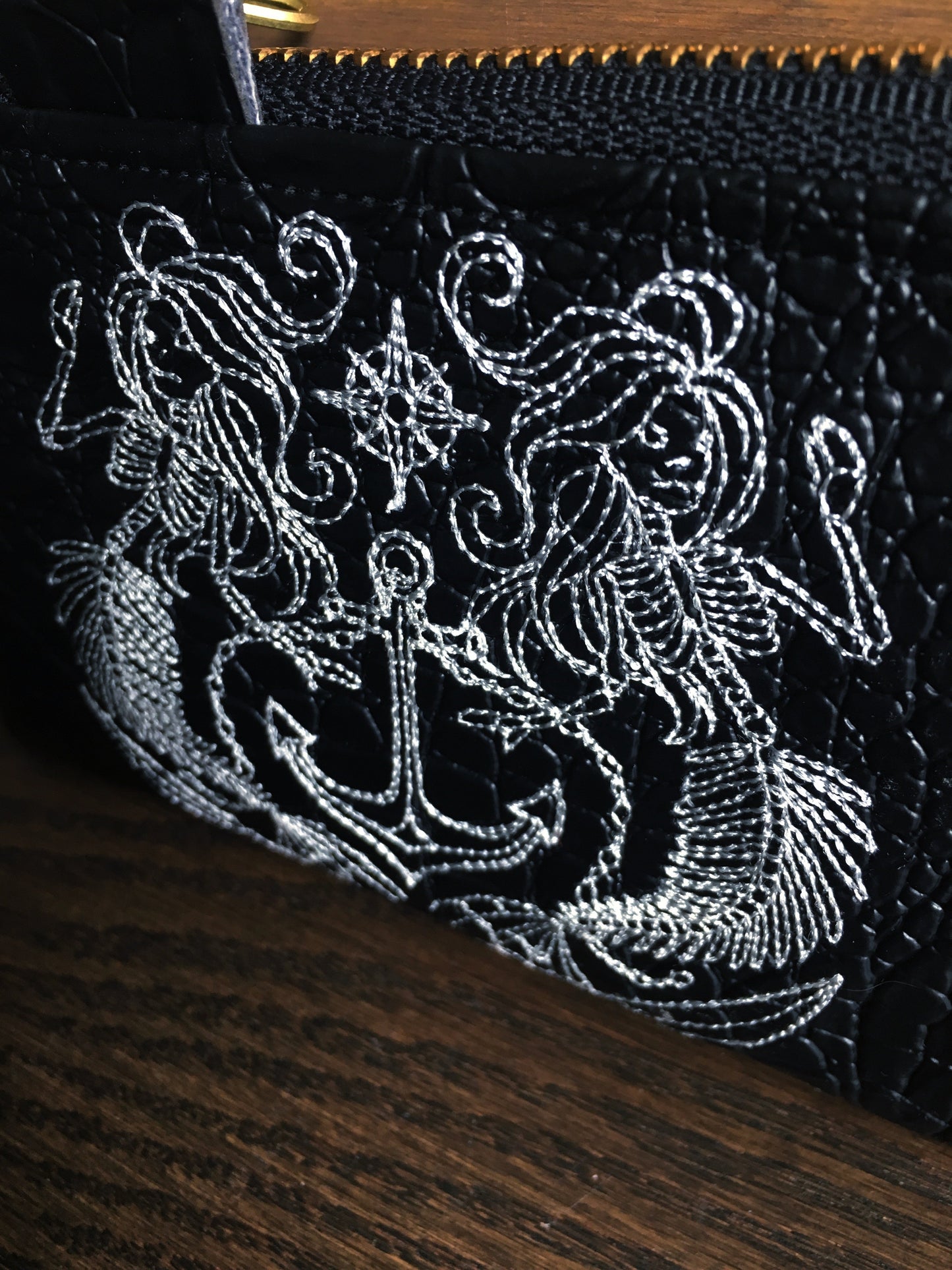 Image of a handmade and pirate themed coin purse featuring a pirate mermaid crest embroidered on faux black alligator leather and backed with beautiful black and white skull and crossbones woven wrap scrap fabric. 
