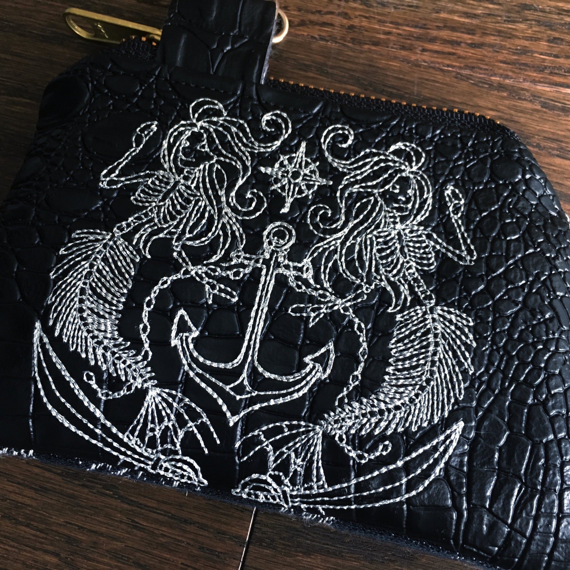 Image of a handmade and pirate themed coin purse featuring a pirate mermaid crest embroidered on faux black alligator leather and backed with beautiful black and white skull and crossbones woven wrap scrap fabric. 