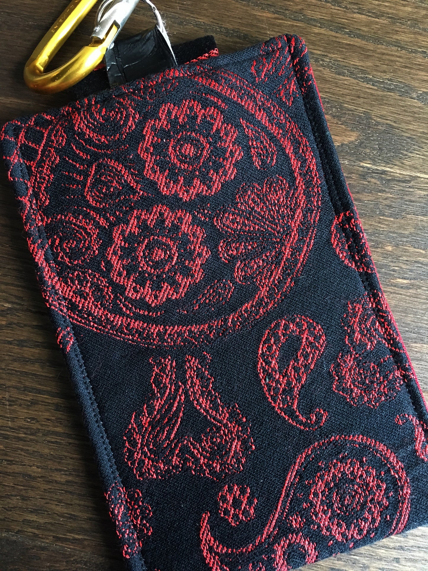 Image of a handmade and pirate themed phone pouch. It features skelewag fabric from Alexander Henry, bold red and black skull and crossbones woven jacquard fabric, an internal card pocket, and a belt or purse clip. 