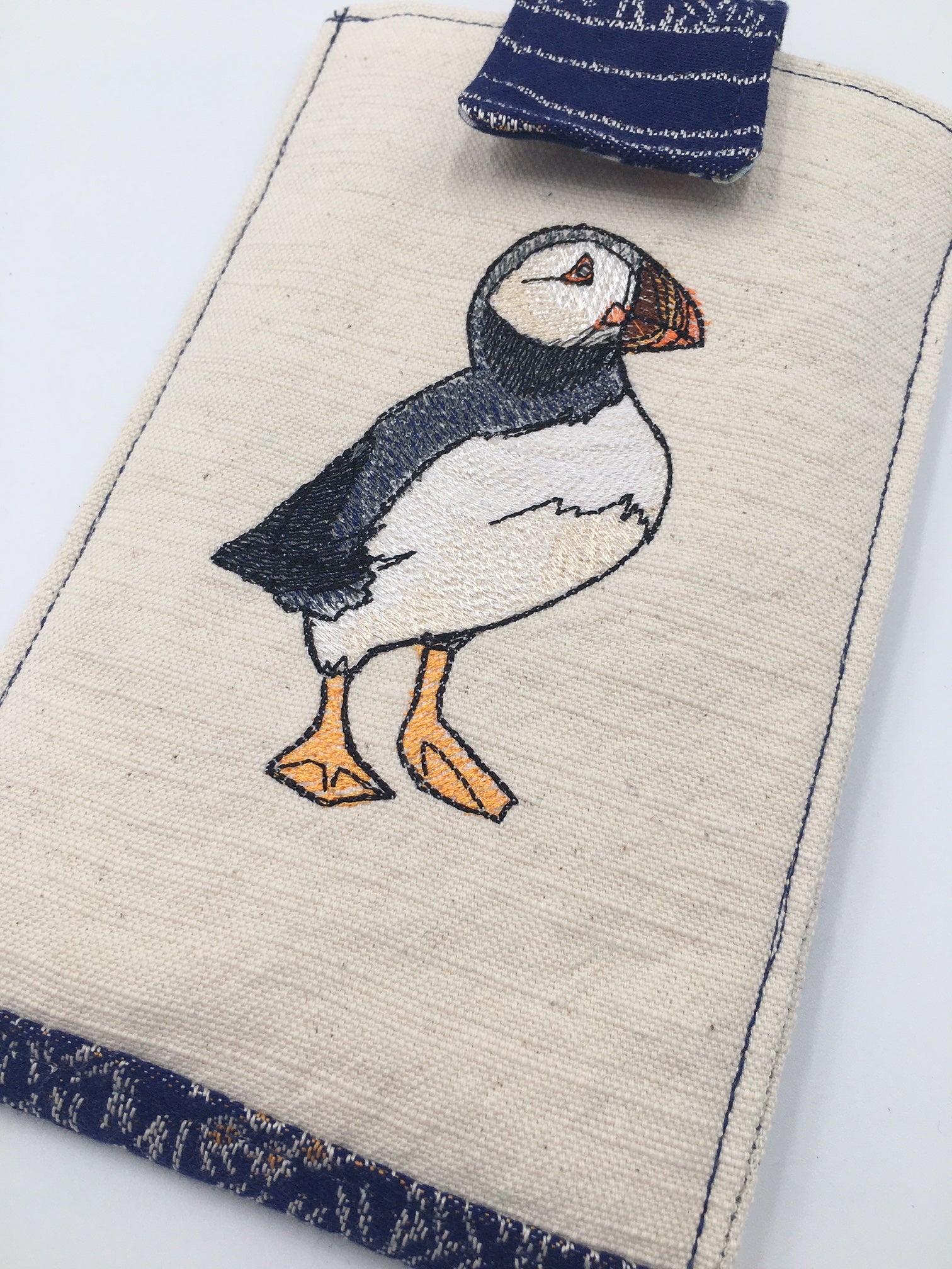 Image of a phone pouch with internal card pocket and belt clip. It features Puffins fabric from Oscha Slings and elegant and realistic puffin embroidery from Urban Threads. 