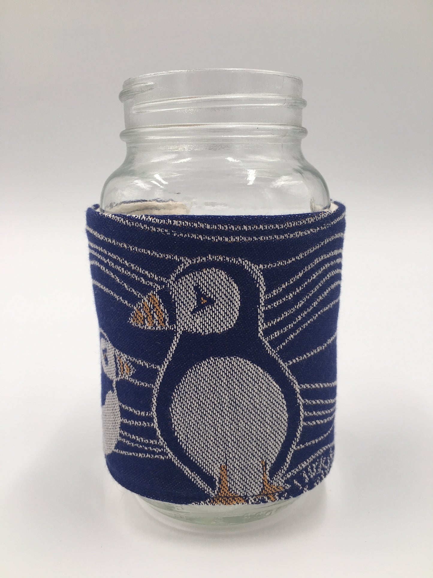 Image of a handmade jar and mug cozy featuring oscha slings puffins woven fabric in deep blue, ivory, and orange and elegant and realistic puffin embroidery. 